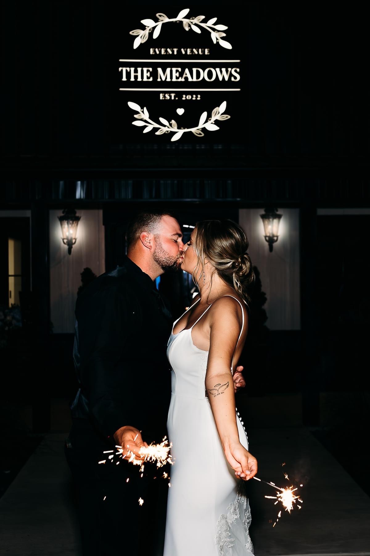 Wedding couple kiss with sparklers in hand at The Meadows Event Venue